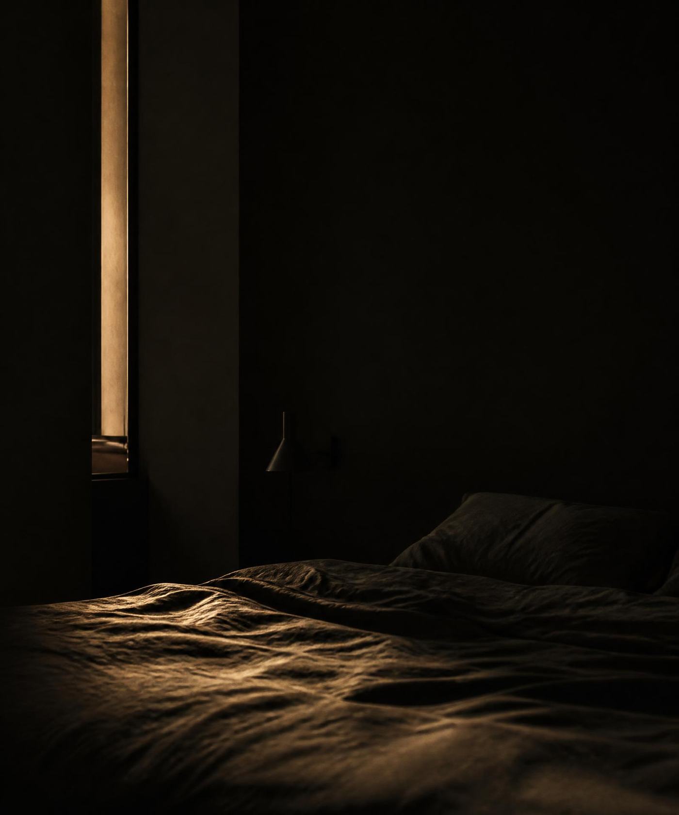 A dark bedroom at night with a thin line of warm light across the linen